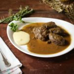 Delicious herb-crusted beef served with gravy and creamy mashed potatoes on a rustic table setting.