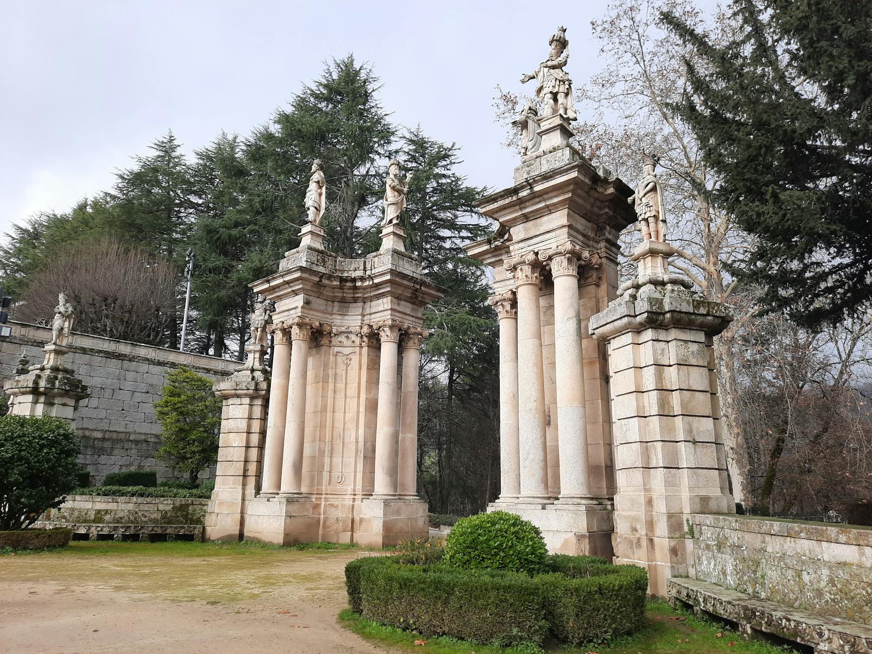Ornate baroque gate with statues in Lamego, Portugal, surrounded by lush greenery.