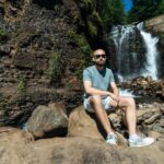 A man sitting on rocks, enjoying a serene waterfall landscape in Гагра, perfect for nature and travel themes.