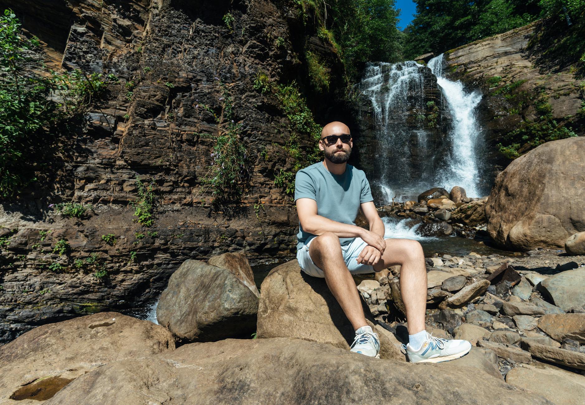 A man sitting on rocks, enjoying a serene waterfall landscape in Гагра, perfect for nature and travel themes.