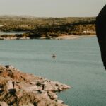Serene view of a lone kayaker paddling on a lake near Capilla del Monte, surrounded by rocky landscape.