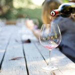 A hand pouring red wine into a glass on an outdoor table, creating a relaxed atmosphere.