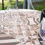Wine bottle and empty glasses on a patterned mosaic table outdoors.