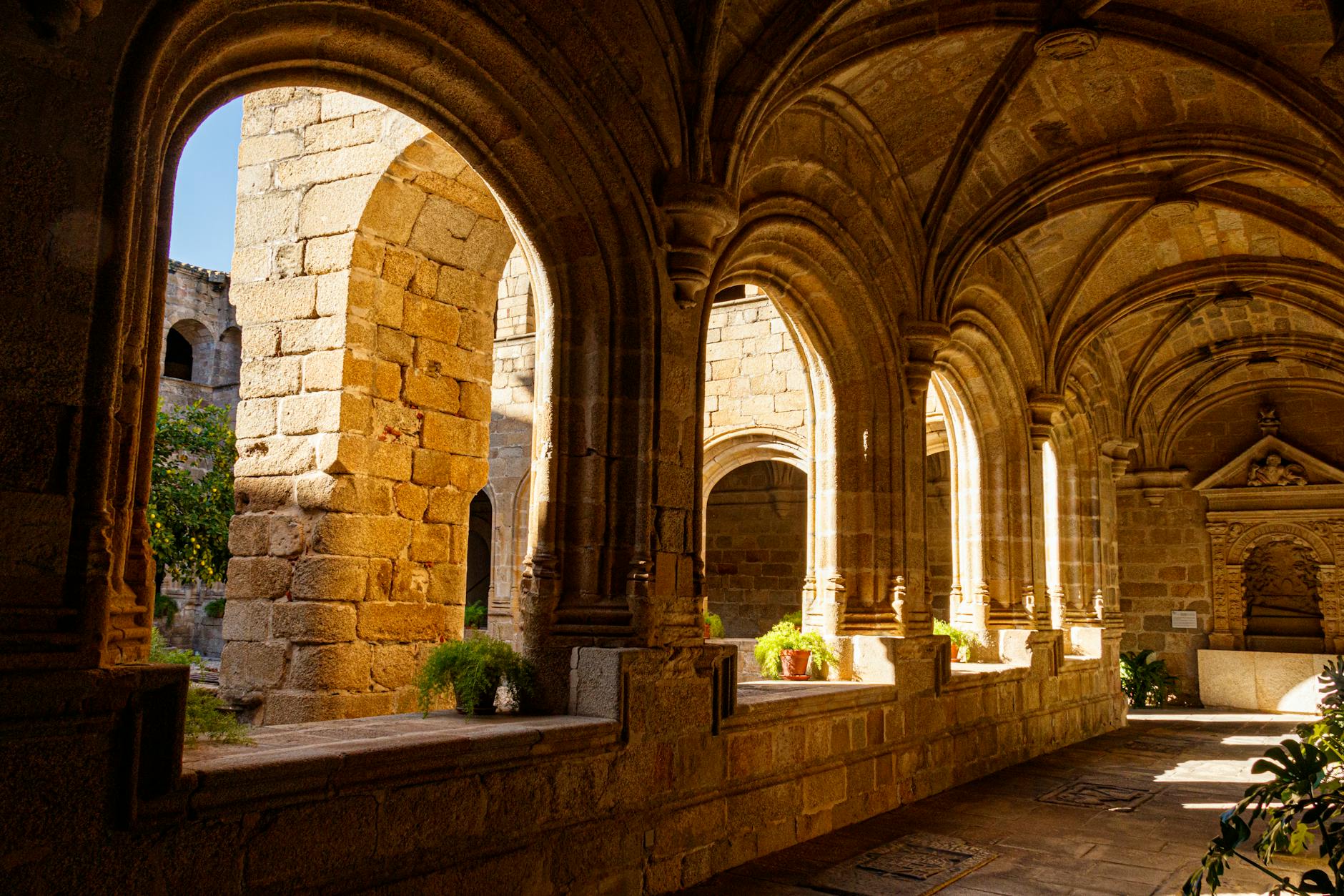 Warm sunlight bathes ancient stone arches in a serene cloister passageway, evoking history and tranquility.
