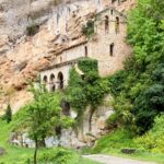 Explore the historic monastery nestled within a lush, green Spanish cliffside setting.