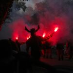 Silhouetted performers with flares create a dramatic scene at a nighttime festival parade.