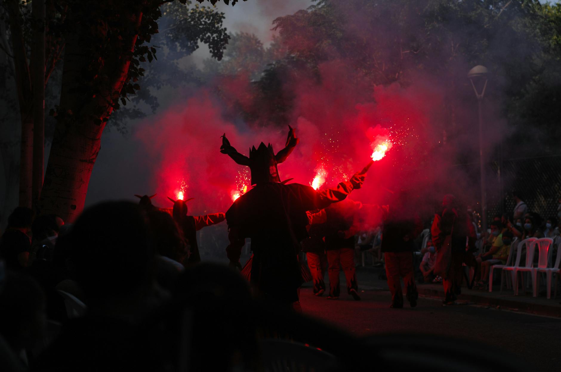 Silhouetted performers with flares create a dramatic scene at a nighttime festival parade.