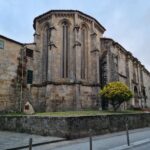 Stone Gothic church exterior with unique architecture and yellow tree.