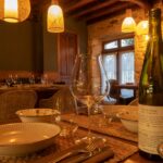 Warm, inviting dining scene with rustic table setting, wine, and elegant tableware in a cozy restaurant.