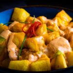 Close-up of patatas bravas with spicy aioli in a vibrant blue bowl.