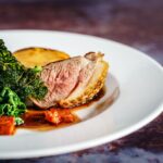 Savor a gourmet duck breast dish with crispy kale and a rich sauce, exquisitely presented on a white plate.