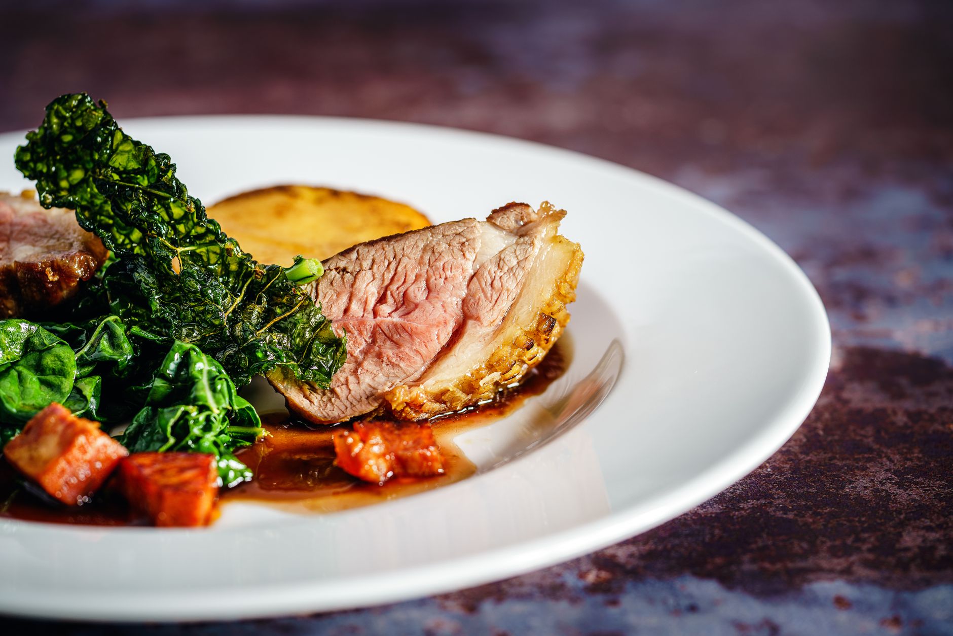 Savor a gourmet duck breast dish with crispy kale and a rich sauce, exquisitely presented on a white plate.