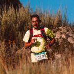 A man participates in a trail marathon, running through rugged terrain in bright sunlight.