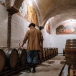A man inspecting wooden barrels in a brewery cellar, checking fermentation storage.