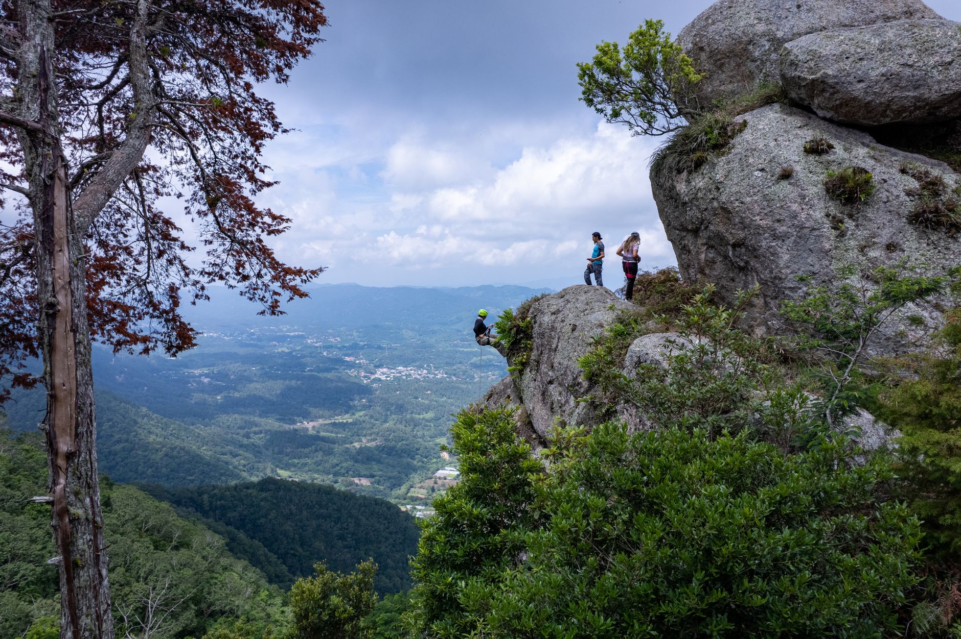 Adventurous rock climbers explore a panoramic cliffside view in El Salvador's lush mountains.