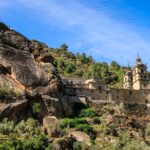 A stunning view of a historic monastery in As Ermidas, Spain, surrounded by lush greenery and rocky hills.