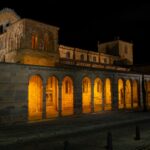 San Vicente Basilica illuminated at night in Ávila, Spain showcasing Romanesque architecture.