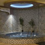 A serene indoor spa setting featuring a mosaic tiled jacuzzi with ambient lighting.