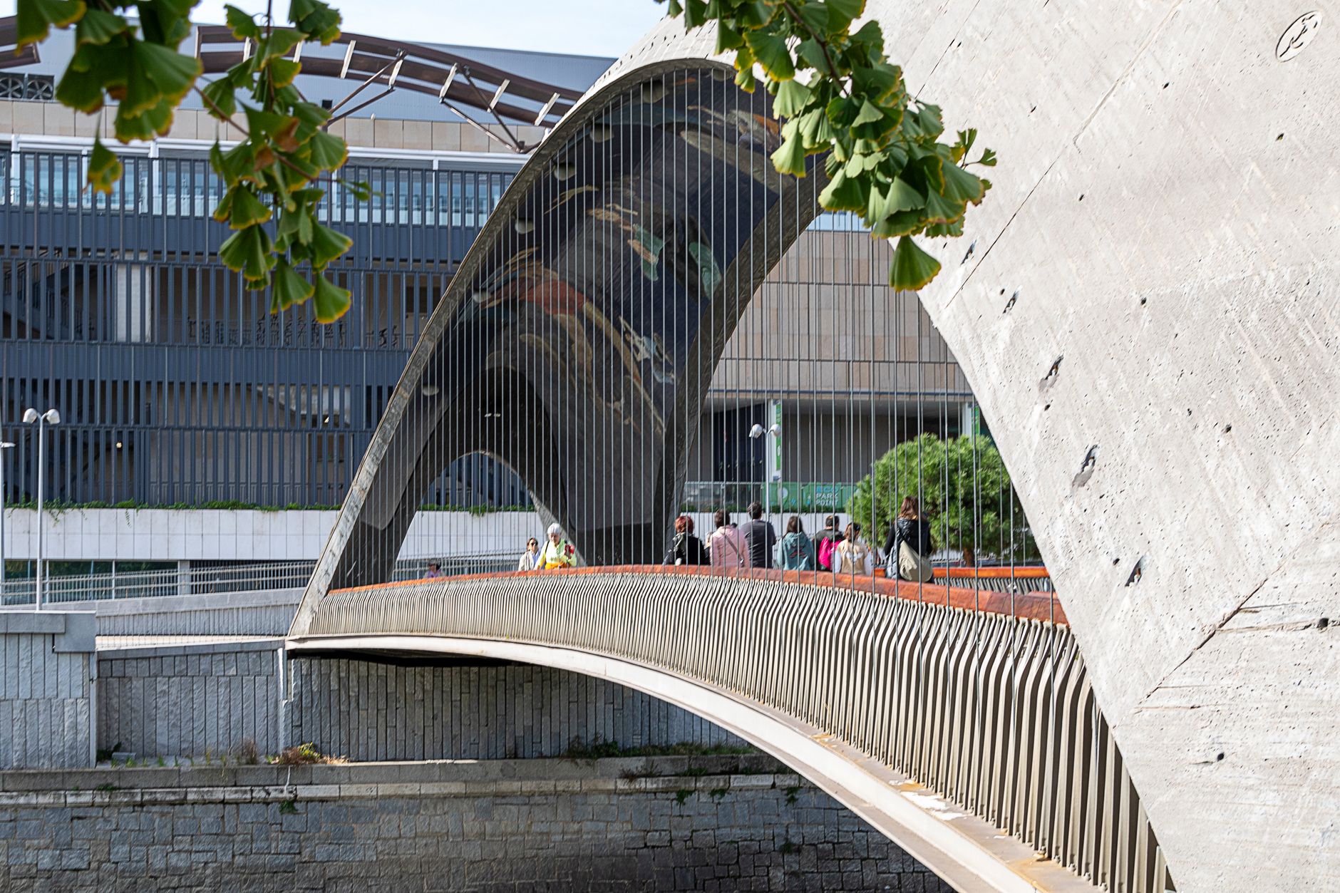 People walking across a modern pedestrian bridge reflecting contemporary architecture in Madrid, Spain.