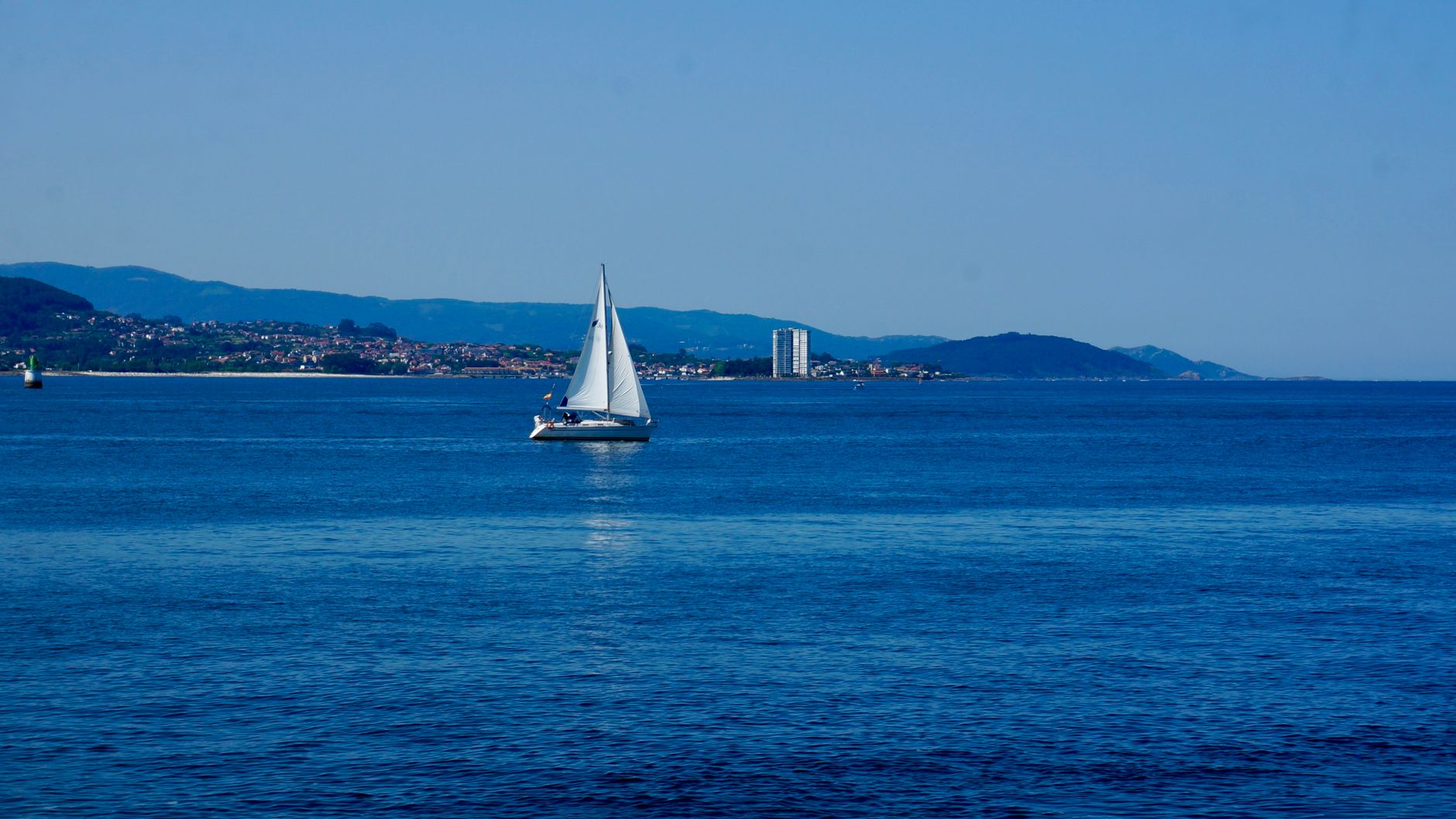 A tranquil scene of a sailboat gliding across the blue waters of Vigo Bay, Spain.