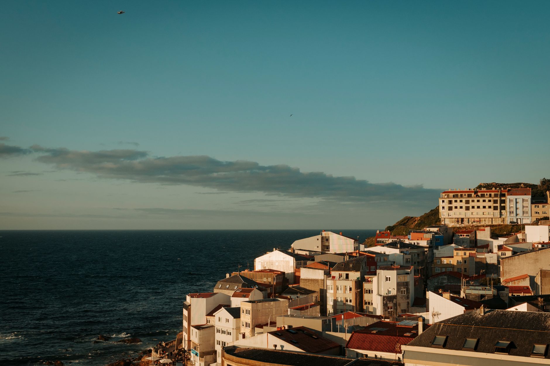 Stunning seaside view of Malpica, Spain with vibrant rooftops and the Atlantic Ocean at sunset.