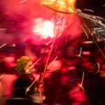 Colorful festival scene with costumed performer holding a sparkling firework, celebrating with motion blur.