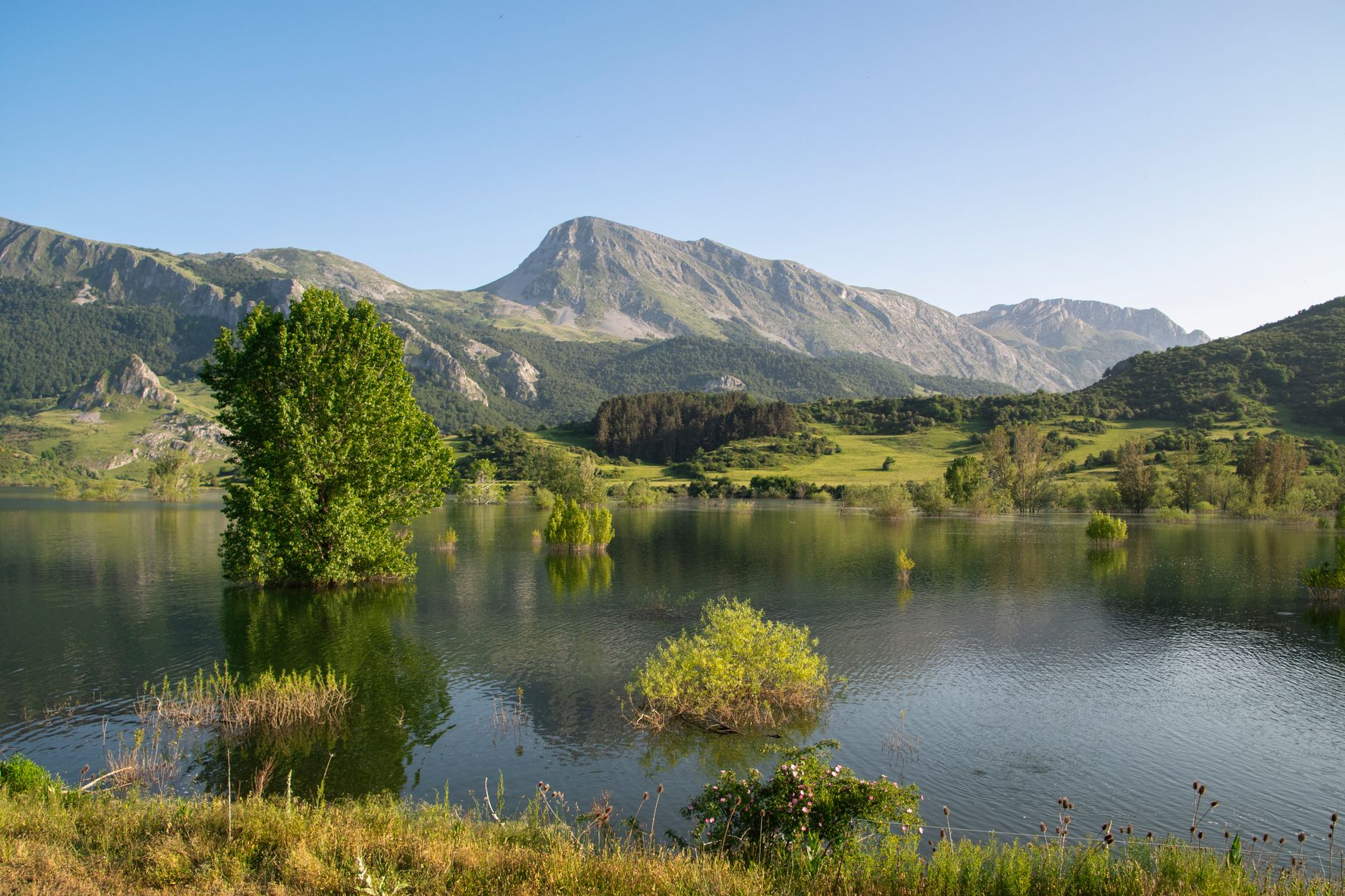 Tranquil mountain lake scene in Burón, Castilla y León, España, showcasing lush greenery and clear skies.