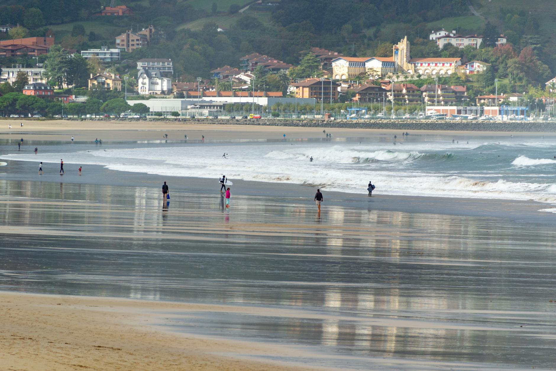 People walking along Playa de Santa Marina with reflections on the wet sand and distant waves.