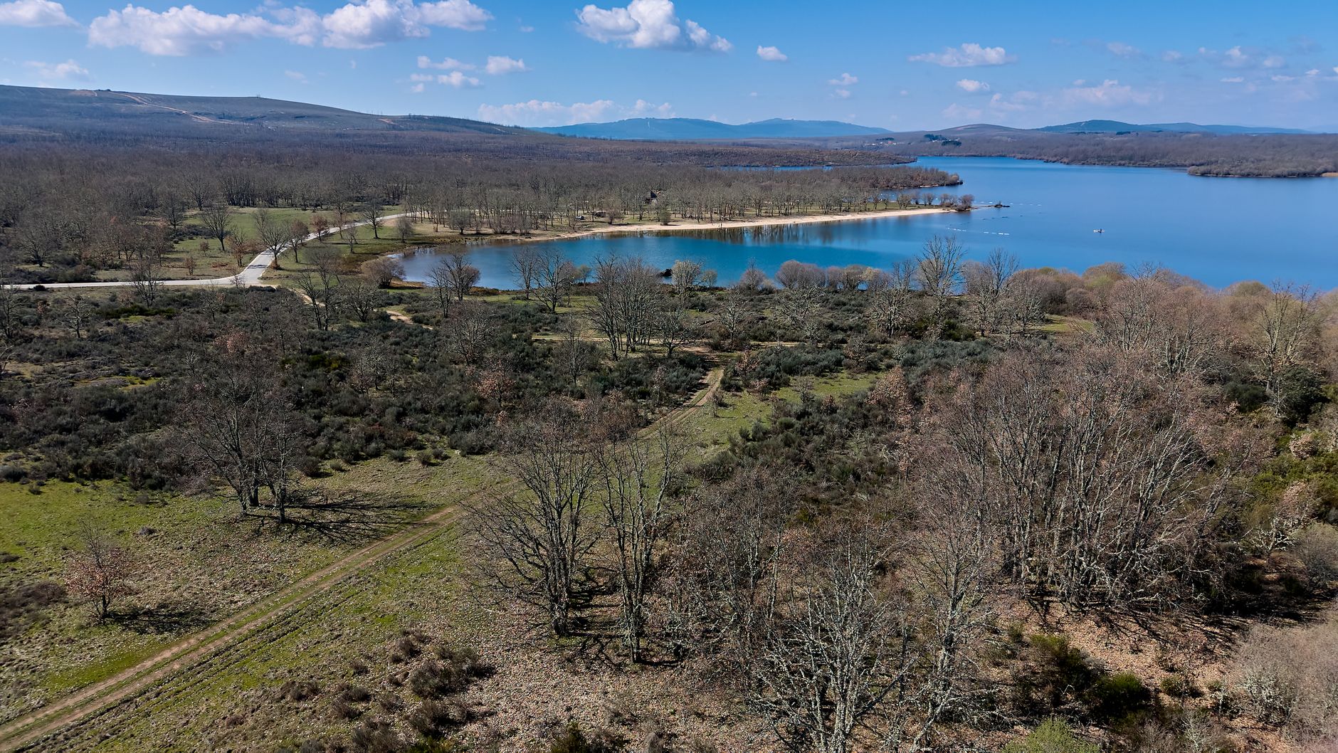 Aerial view of a serene lake and wooded area in Zamora, Spain, under a bright blue sky.
