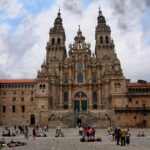 Tourists gather at the historic Santiago de Compostela Cathedral in Spain under a cloudy sky.
