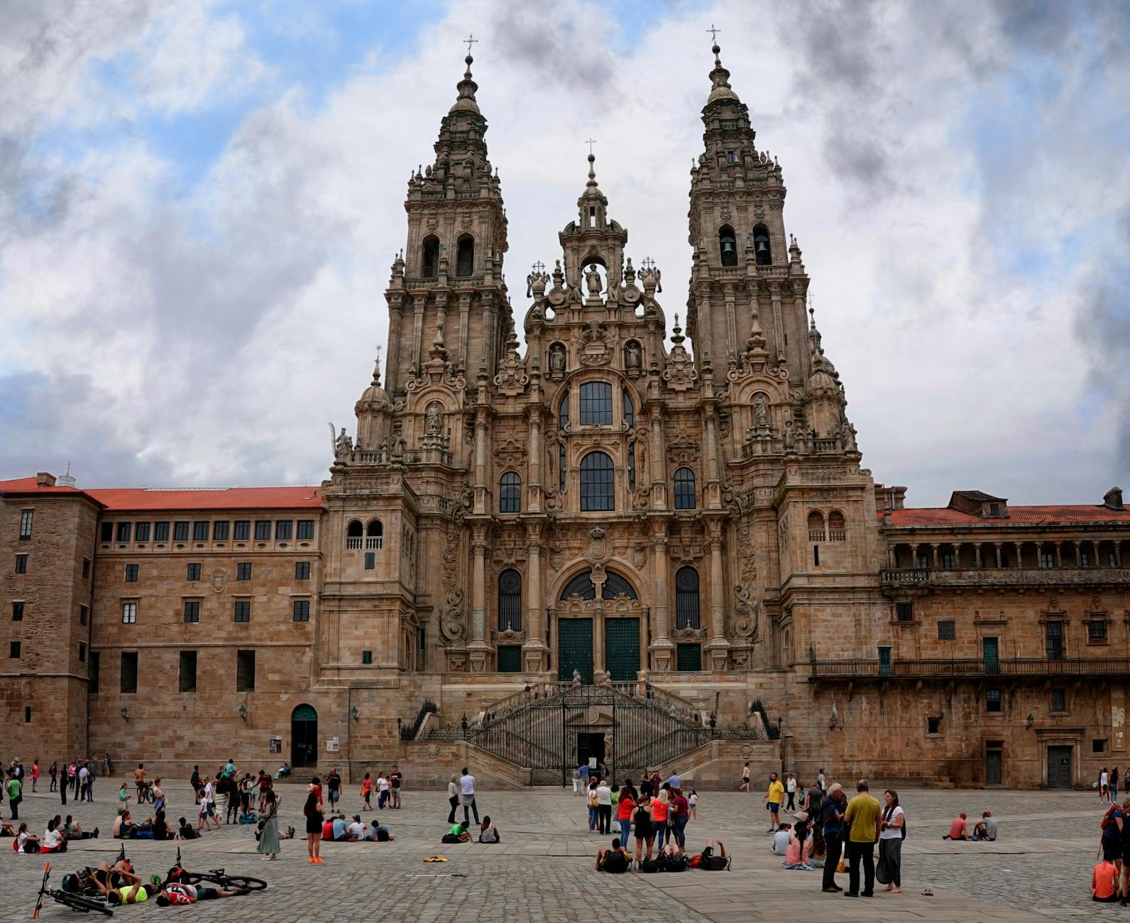 Tourists gather at the historic Santiago de Compostela Cathedral in Spain under a cloudy sky.