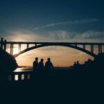 Silhouetted people against a sunset backdrop under Porto's iconic bridge, Portugal.