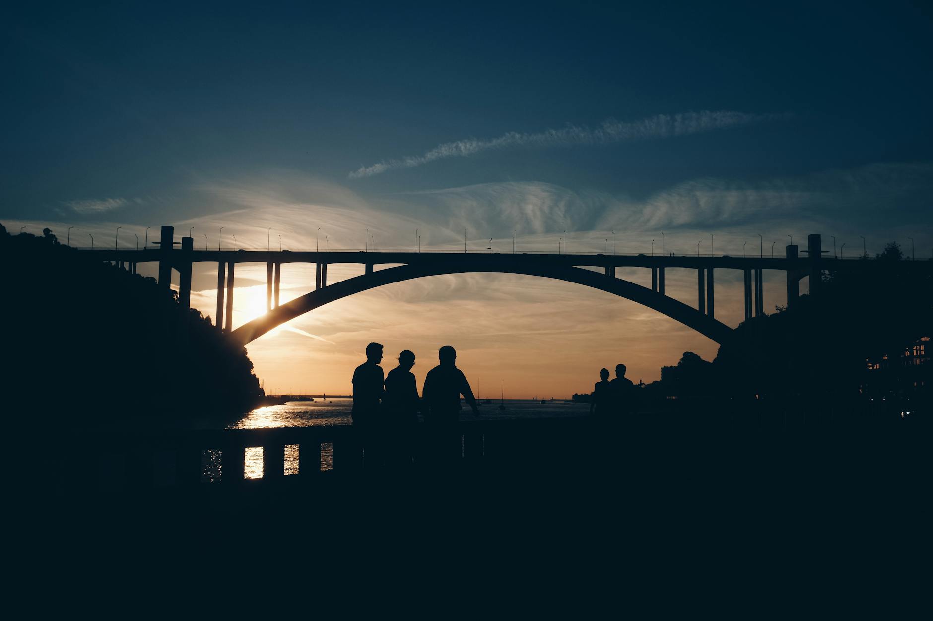 Silhouetted people against a sunset backdrop under Porto's iconic bridge, Portugal.