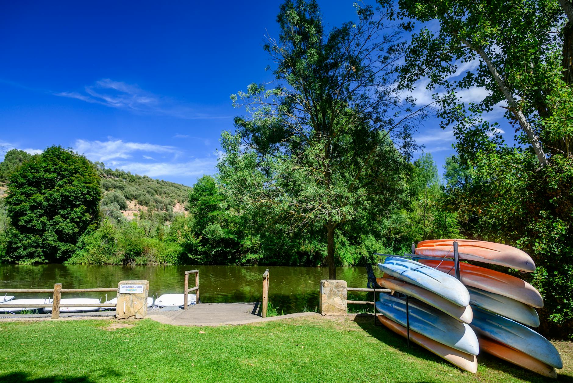 Colorful kayaks stacked by the Duero River in Soria, Spain on a sunny day, perfect for outdoor adventures.