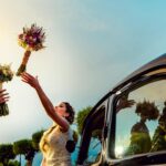 Two brides joyfully exchange bouquets beside a vintage car at their vibrant wedding in Toledo.