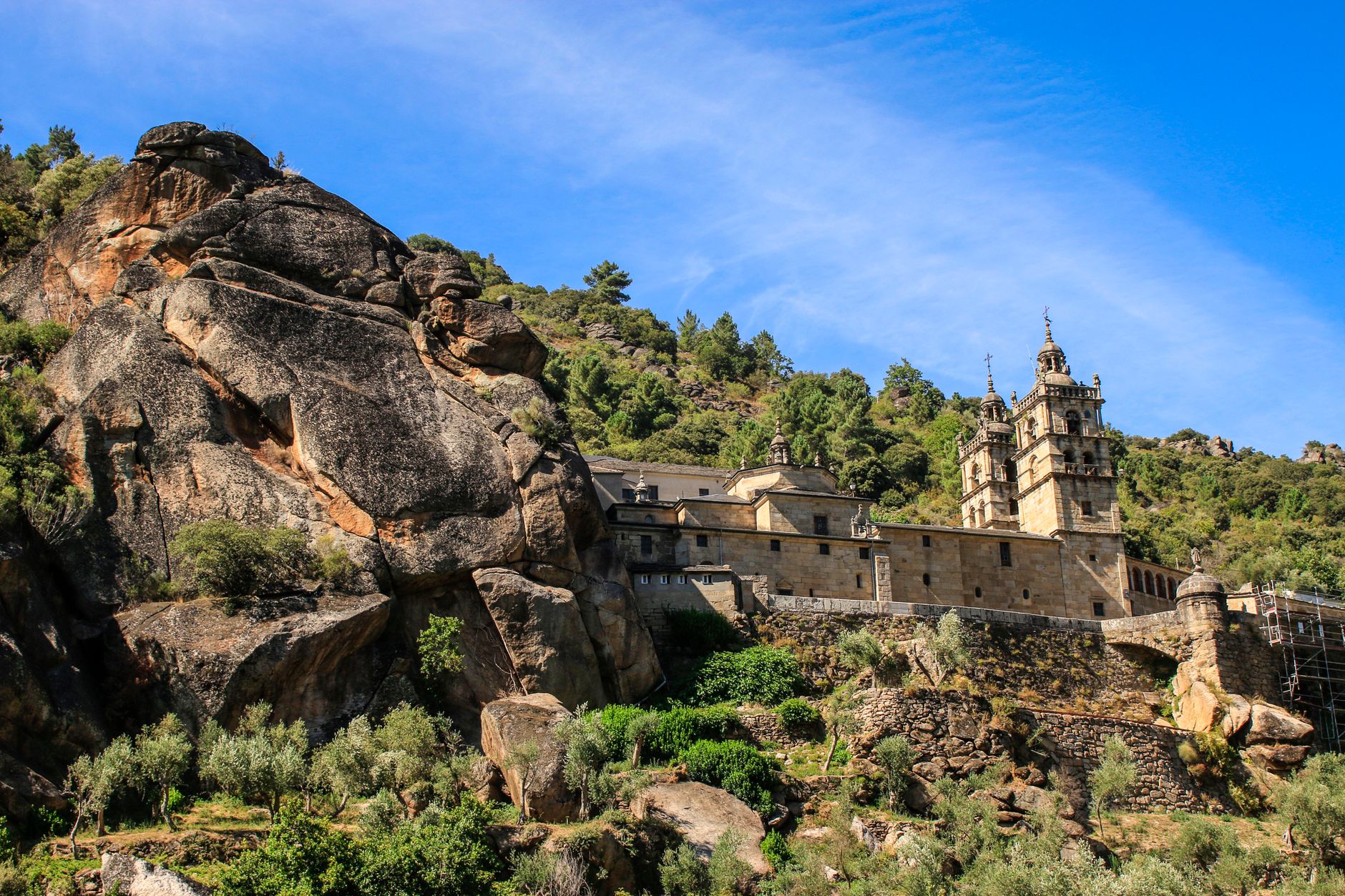 A stunning view of a historic monastery in As Ermidas, Spain, surrounded by lush greenery and rocky hills.