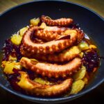 A mouthwatering dish of grilled octopus garnished with vegetables served in a skillet.
