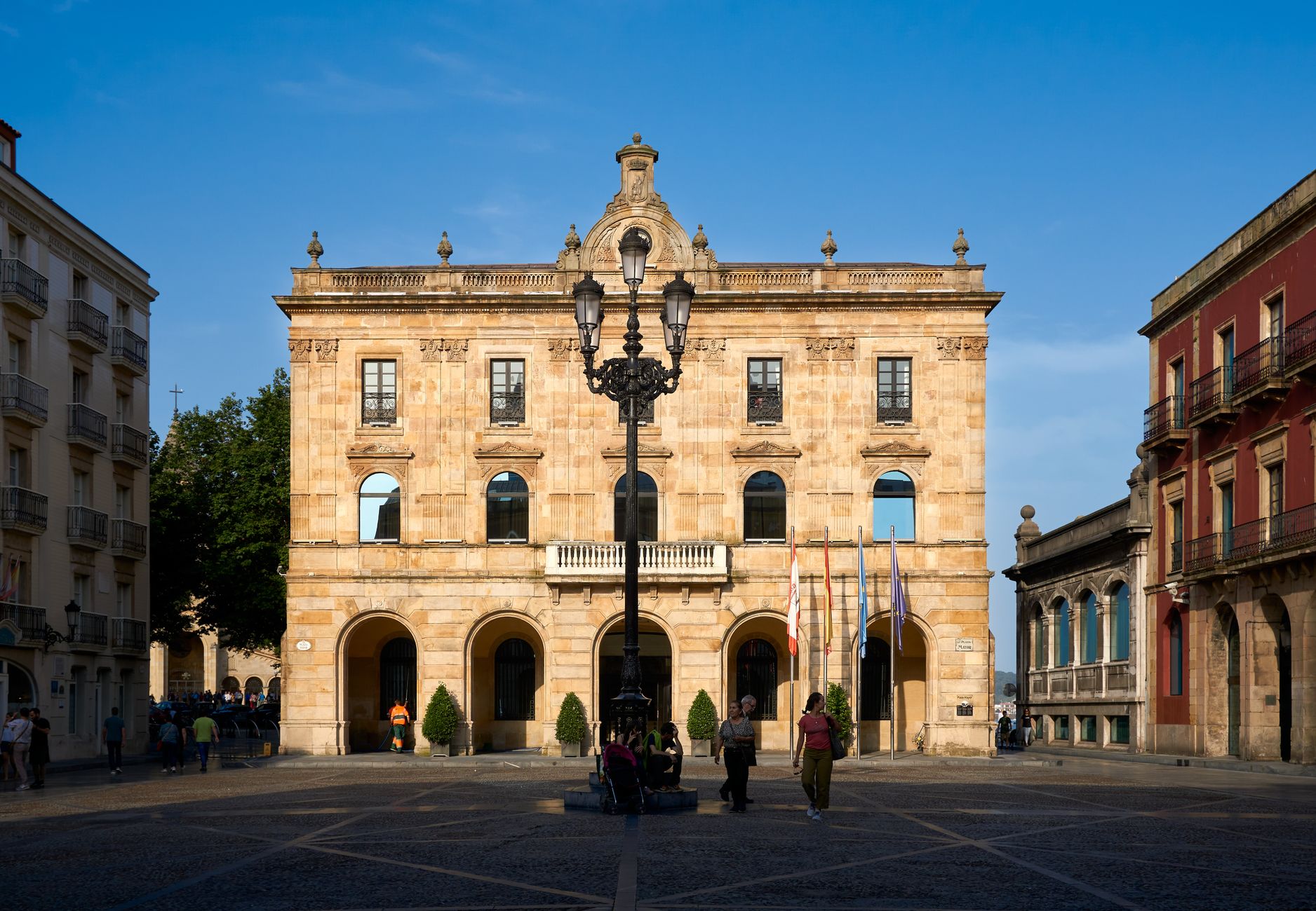 A vibrant view of a historic city hall in Gijon, Spain, under a blue sky. Architecture with a street scene.