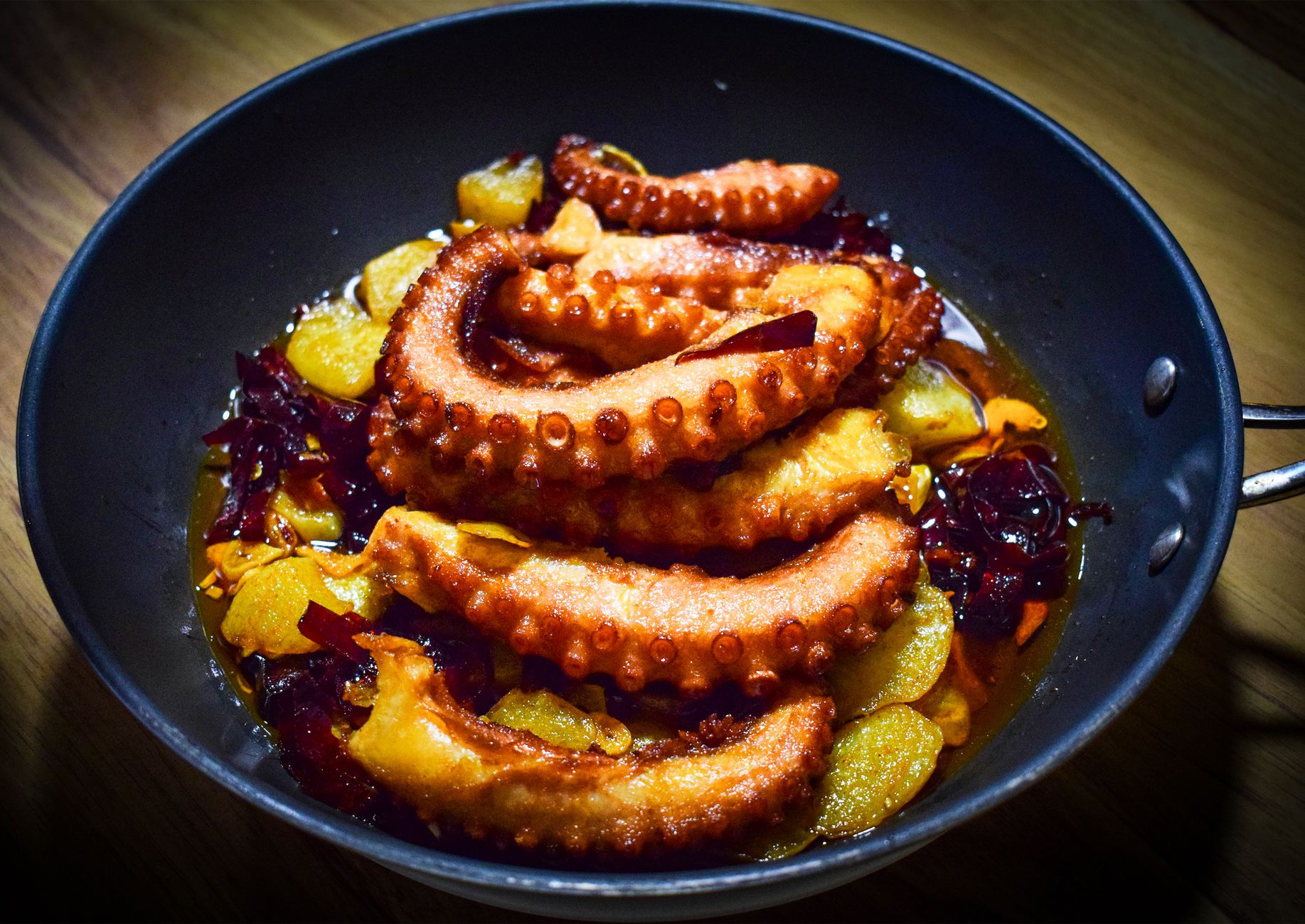 A mouthwatering dish of grilled octopus garnished with vegetables served in a skillet.