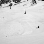 A lone skier sits on a snowy mountain slope under a clear sky, capturing winter's tranquility.