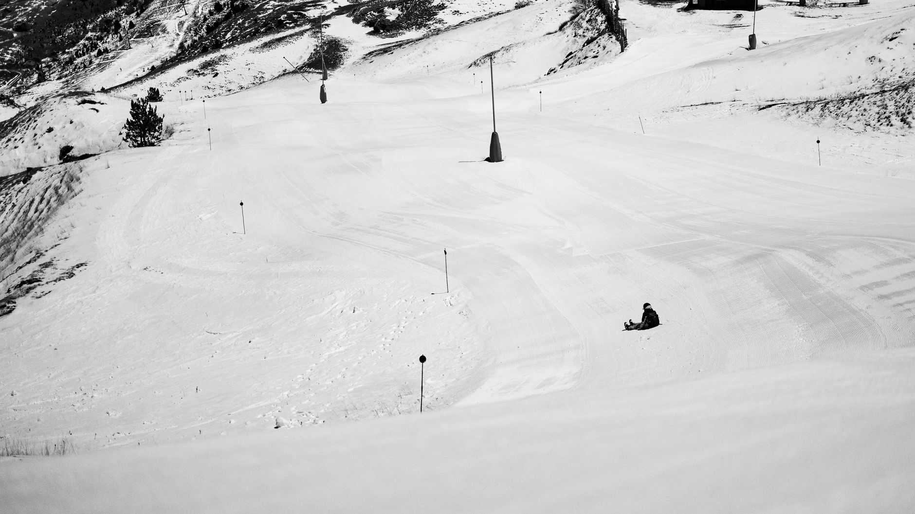 A lone skier sits on a snowy mountain slope under a clear sky, capturing winter's tranquility.